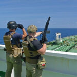 Armed security team on a ship deck overlooking a large tanker at sea