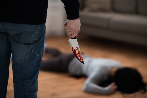 A person holding a bloody knife stands over a victim lying on the floor