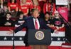 Man speaking at a rally with crowd behind.