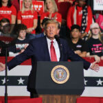 Fourth Of July Firebomb: Communism Named Threat Man speaking at a rally with crowd behind.