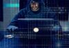 Person in hoodie using a laptop with binary code overlay
