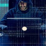 Phone Fraud Kingpins Just Hit a Wall Person in hoodie using a laptop with binary code overlay