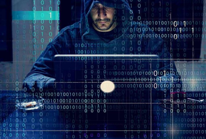 shutterstock_1066763072 Person in hoodie using a laptop with binary code overlay