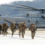 Soldiers disembark and walk past a large military helicopter