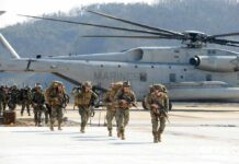Pentagon Quietly Revises Iran War Injury Toll Soldiers disembark and walk past a large military helicopter