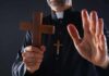Clergyman holding wooden cross with hand raised