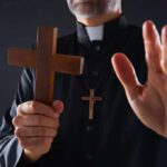 Clergyman holding wooden cross with hand raised