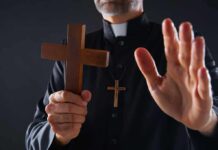 Clergyman holding wooden cross with hand raised