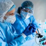 Scientists in protective gear working with a syringe in a laboratory