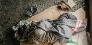 Person sleeping on cardboard with a blanket outdoors.