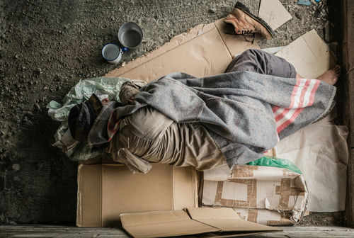 Person sleeping on cardboard with a blanket outdoors.