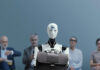 Robot holding a briefcase sits among human job candidates