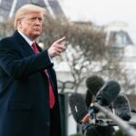 A man in a suit gesturing while speaking at a press conference outside the White House
