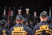 Navy officers stand at attention on stage during a ceremony