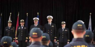 Navy officers stand at attention on stage during a ceremony