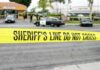 yellow sheriff's line tape blocks a street near police cars