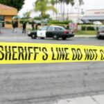 yellow sheriff's line tape blocks a street near police cars
