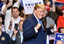 man in suit raising fists at a rally podium
