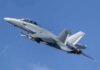Twin-engine fighter jet climbing in a clear blue sky