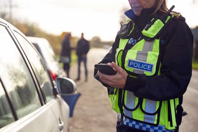shutterstock_1937024641 Police officer using a smartphone during a roadside stop