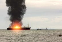 Cargo ship on fire with thick black smoke at sea