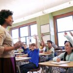 Teacher engaging with students raising hands in a classroom