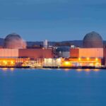 Nuclear Giant Kneels To A River nuclear power plant with two domed reactor buildings by water at dusk
