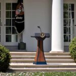 Republican Blasts Trump’s $1.8B Payout Plan Podium with presidential seal in a garden colonnade