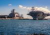 Aircraft carrier and support ships docked at a naval harbor