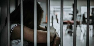 Person sitting behind jail bars with head down