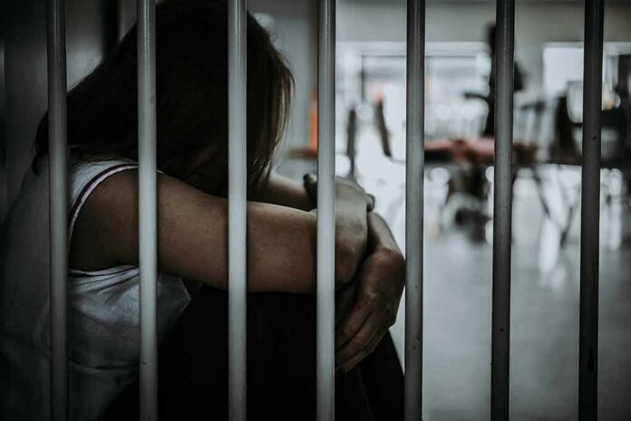 Person sitting behind jail bars with head down