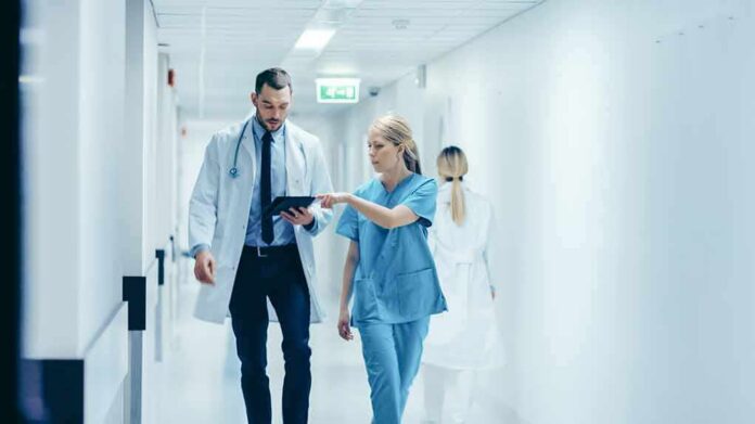 shutterstock_1189798168 Doctors walking in a hospital corridor reviewing a tablet