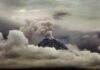 Volcano erupting with ash plume above cloud layer