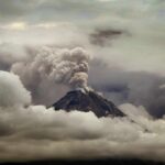 Volcano erupting with ash plume above cloud layer