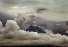 Volcano erupting with ash plume above cloud layer