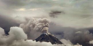 Volcano erupting with ash plume above cloud layer
