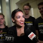 Woman speaking to reporters with microphones surrounded by supporters
