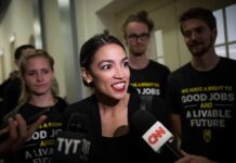 Woman speaking to reporters with microphones surrounded by supporters