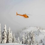 Yellow helicopter flying over snowy forested mountains