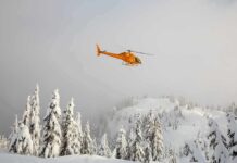 Yellow helicopter flying over snowy forested mountains