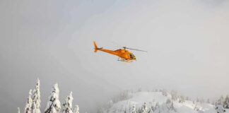 Yellow helicopter flying over snowy forested mountains