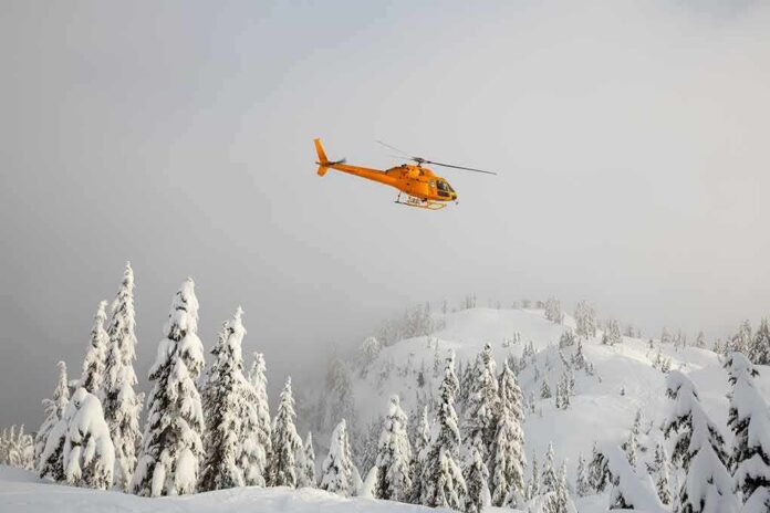 Yellow helicopter flying over snowy forested mountains