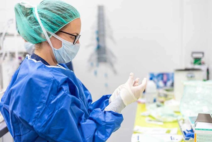 medical professional in blue gown putting on sterile gloves