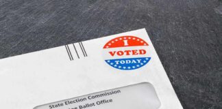 Absentee ballot envelope with I Voted sticker on dark surface