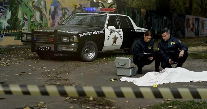 shutterstock_1709493973 Crime scene with police car and two investigators by a covered body