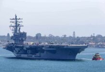 Aircraft carrier escorted by a tugboat in a harbor
