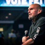 Bald man in a hoodie speaking into a microphone on stage
