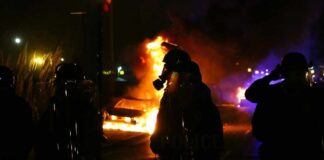 Riot police stand near burning cars at night