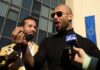 Two men speaking to reporters with microphones outside a modern building