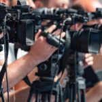 Oil Jugular Exposed — One Hit, Chaos television cameras on tripods at a media event